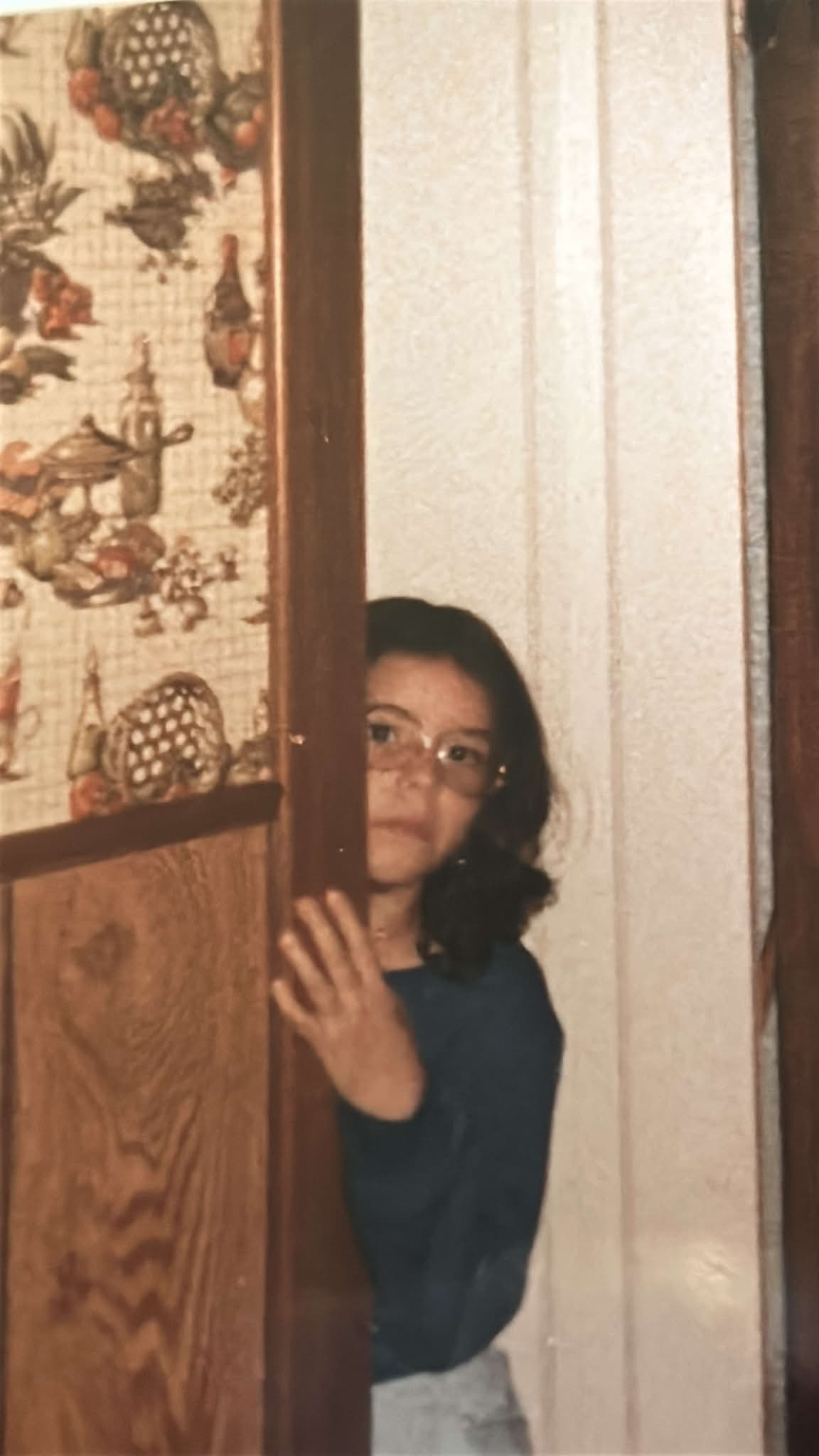 CeCe Moreno as a child peeking from behind a wooden cabinet